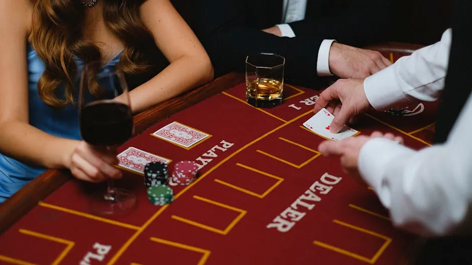Close-up of a card game with players and chips at a casino table, featuring wine and whiskey glasses.