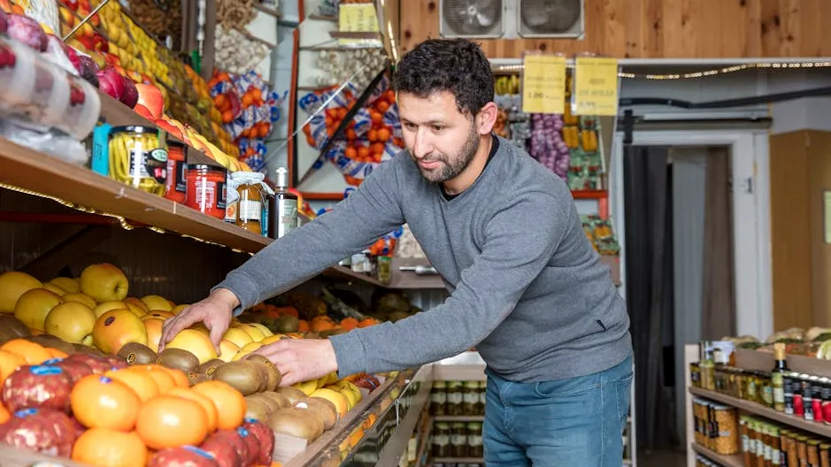 Grocery store worker organizing fresh fruits and vegetables on display shelves.