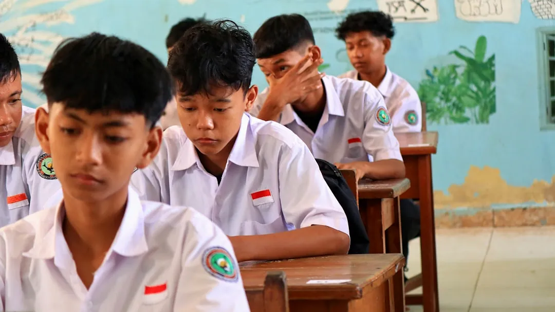 Students in white uniforms sitting at desks in classroom.