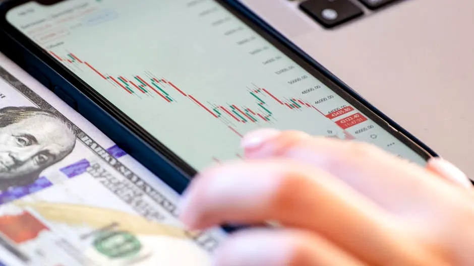 Close-up of a smartphone displaying stock market data over a dollar bill on a desk.