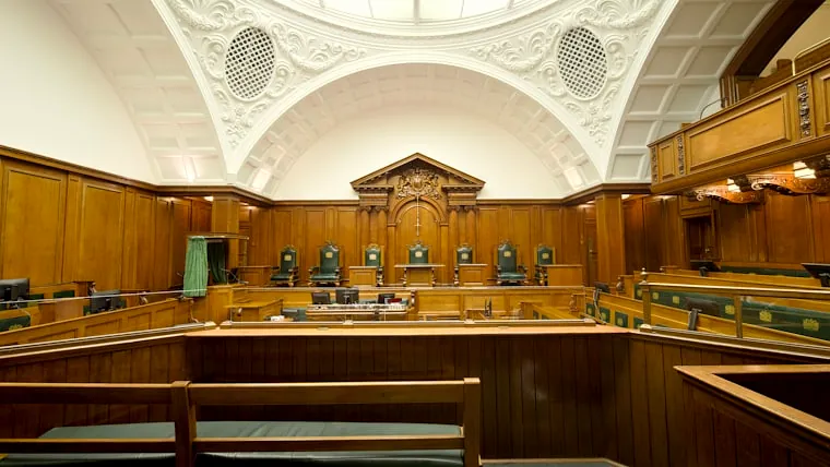 Empty courtroom featuring rich wooden paneling and a decorative ceiling.